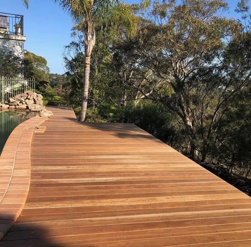 Timber walkway with a brick edging next to a water feature and trees near a home